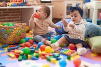 zwei-kleinkinder-spielen-mit-baellen-und-xylophon-auf-dem-boden-im-kindergarten-min